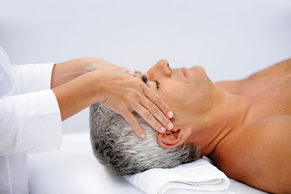 An older man receiving a head massage while lying on a massage table