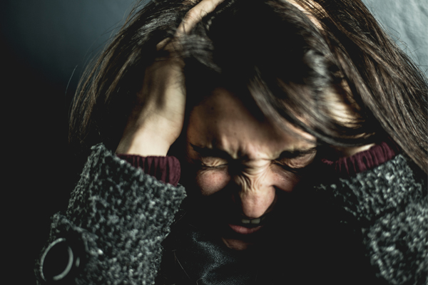 Woman holding her head in extreme pain from migraine headache.