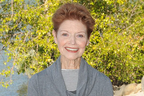 Judith Aston, who partnered with Dr. Ida Rolf, poses for a picture in front of a backdrop of trees and a lake.