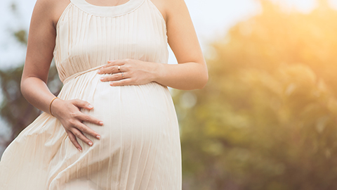 Pregnant woman outdoors with her hands on belly