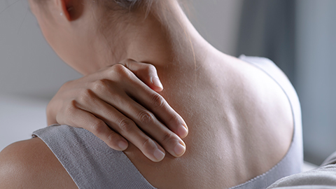 A view of a woman holding her left shoulder with her right hand looking downward.