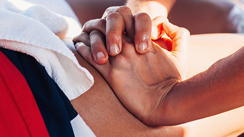 A pair of hands applying pressure to an athletes hamstring.