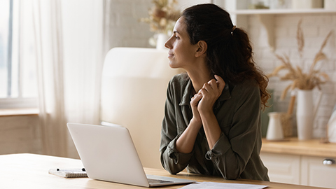 A thoughtful woman working on her laptop looking out the window.