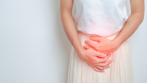 A woman holding her lower abdomen with red pain coloring.