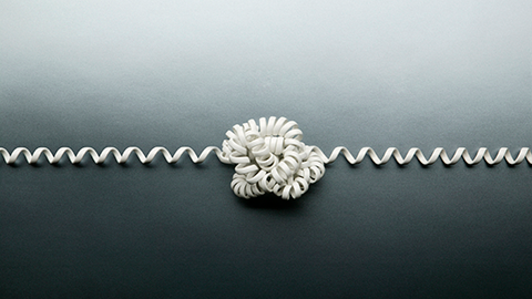 Coiled telephone cord tied in a knot on gray background.