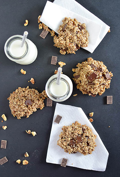 An array of dark chocolate oatmeal cookies with glasses of milk 