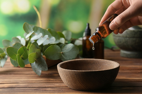 Essential oils being poured into a bowl for aromatherapy.