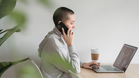 A person sits at their desk talking on their phone while working on a computer.