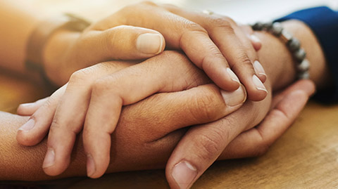 Two hands interlocked resting on a wood table.