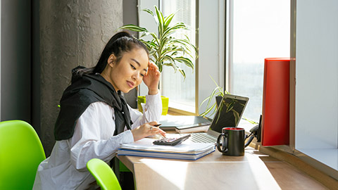 A woman sitting at her desk using a calculator for tax preparation.