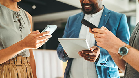 3 people standing around on their smartphones and tablets.