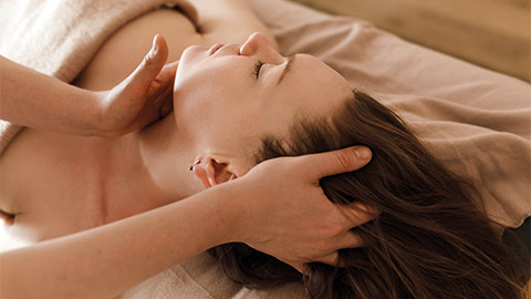 A woman receiving bodywork to her neck and head.