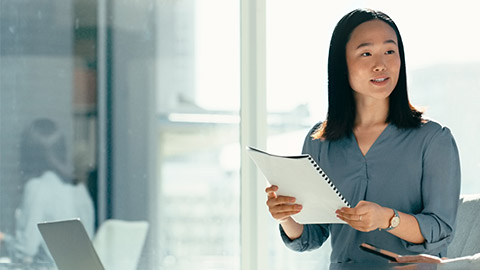 Image of a woman presenting at a meeting holding a notebook.