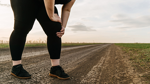 An overweight woman holding a painful leg during an outdoor run