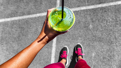 POV of a person looking down at their shoes and a green smoothie.