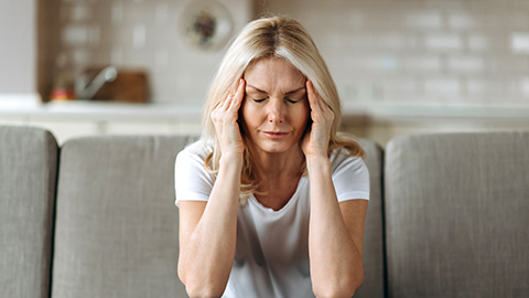 A woman with a migraine sitting on her couch rubbing her temples. 