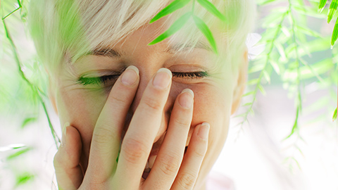 Young woman smiling with hand on her face, underneath leaves