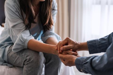 Two people hold hands, with one of them consoling the other.