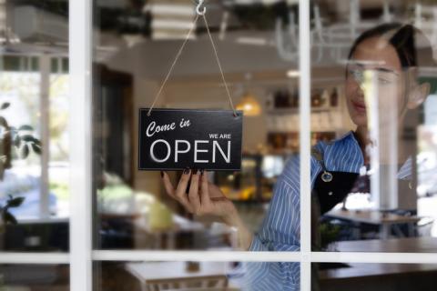 A woman hangs a sign that reads 'Come in we're open' in a window at a business.