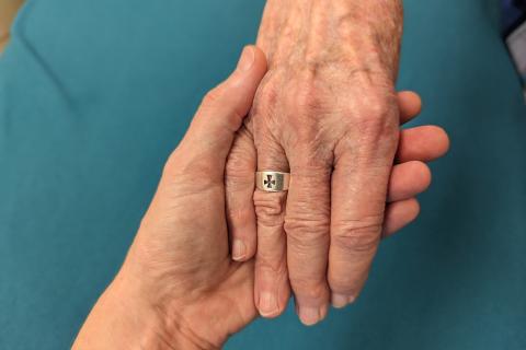 One hand supports another that bears a ring with a cross on the ring finger.