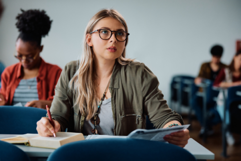 A woman in a classroom takes notes while looking forward.