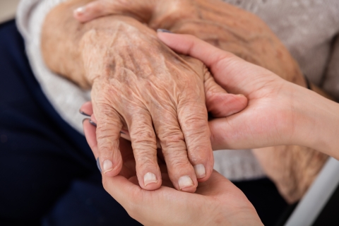 A pair of hands holds the hand of an older person.