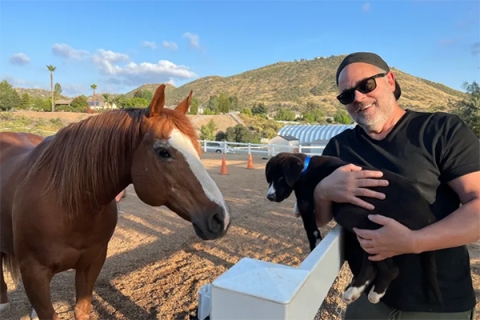 Chris Kincade smiles for a picture while standing next to his horse and holding a puppy.