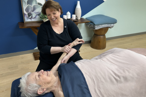 A massage therapist tends to a senior client's left arm.