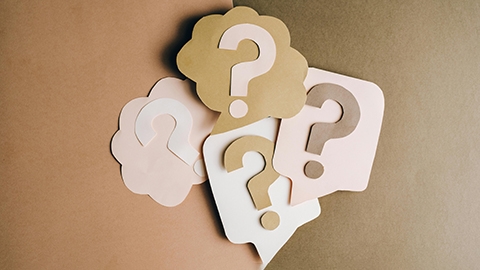 Image of cut out cards with question marks against a tan background.
