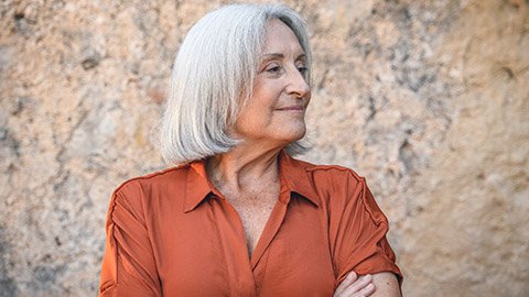 An older female massage therapist smiling with her arms crossed.