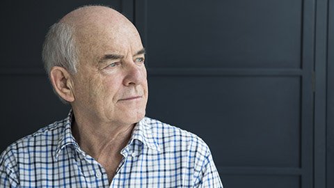 An image of an elderly man looking off in the distances against a navy blue background.