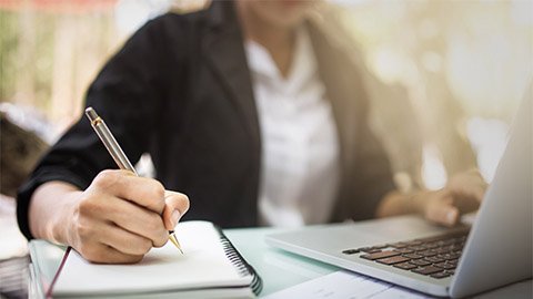 An image of a person working on their laptop and using a spiral notebook.