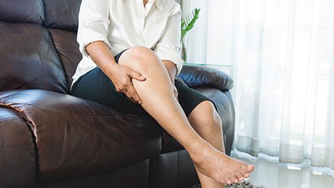 A woman rubbing her calf muscle while sitting on the couch.