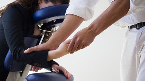 Massage therapist massaging seated client's forearm during chair massage.