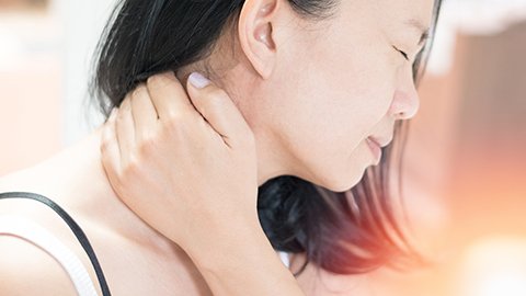 Asian woman rubbing her neck in pain.