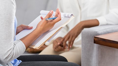 Massage therapist with a clipboard performing intake with a client.