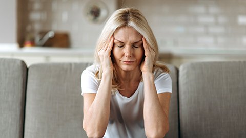 A woman with a migraine sitting on her couch rubbing her temples. 