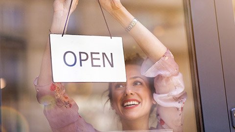 Smiling woman hanging an "Open" sign in a shop window