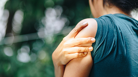 A woman standing outdoors holding a painful shoulder